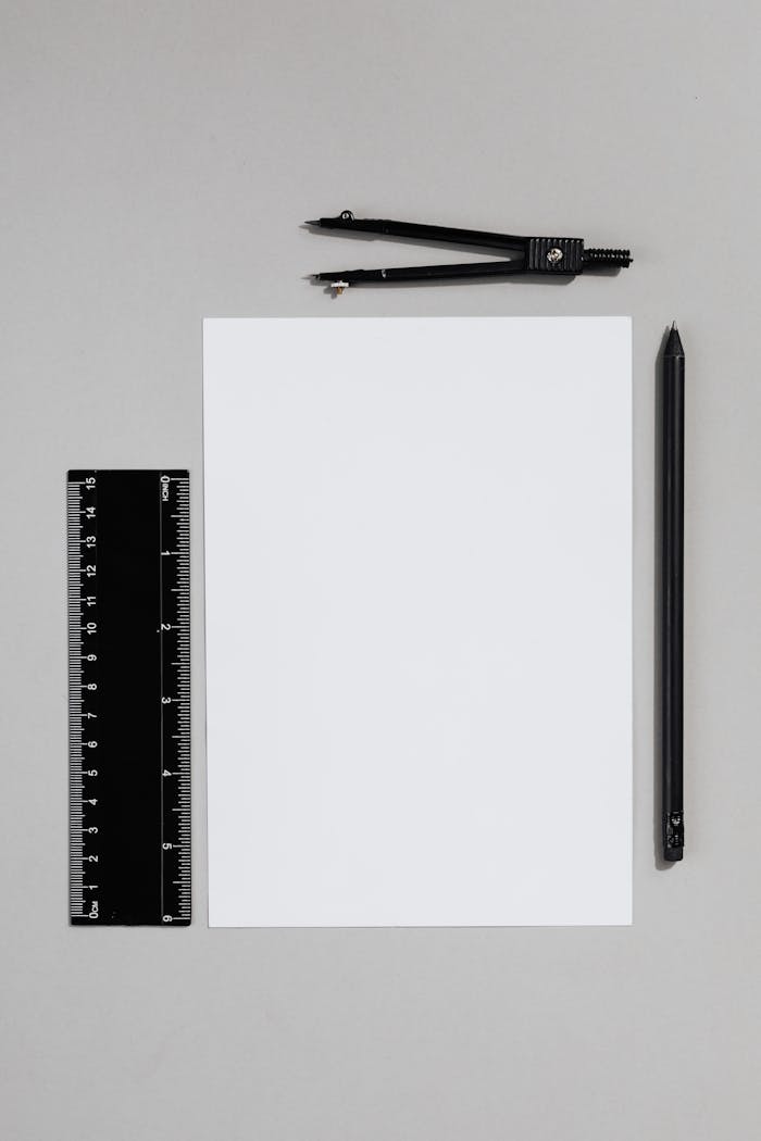 Flat lay image of school supplies including a compass, pencil, and ruler on a gray background.